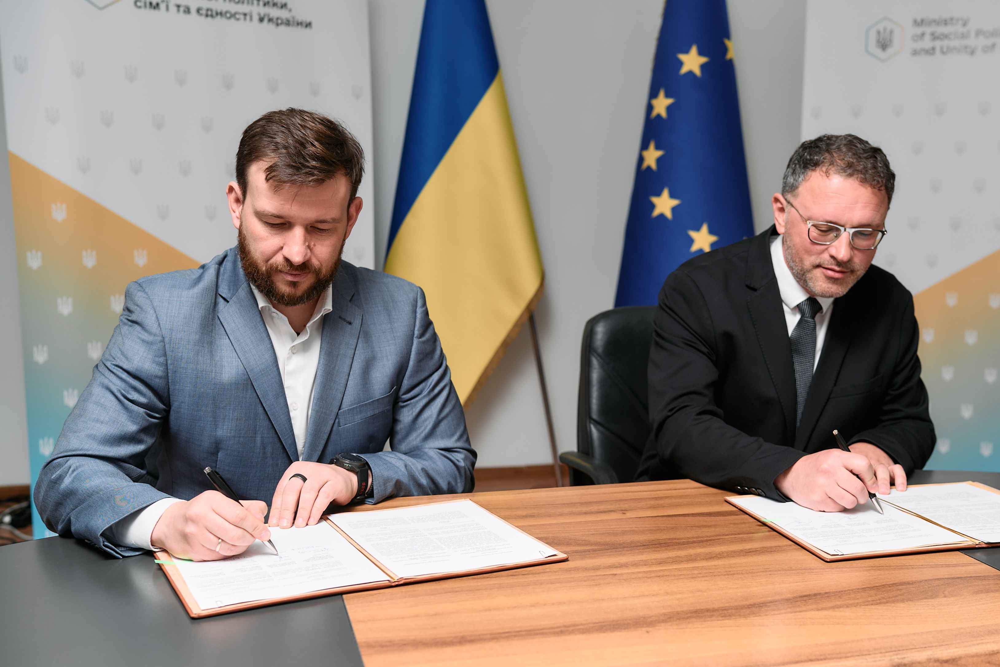 На фото чоловіки сидять за столом і підписують документи На фото чоловіки сидять за столом і підписують документи