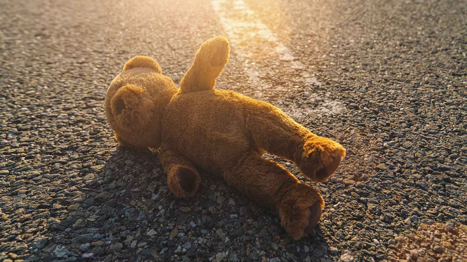 На фото зображено дитячу іграшку ведмедика. який лежить на асфальті