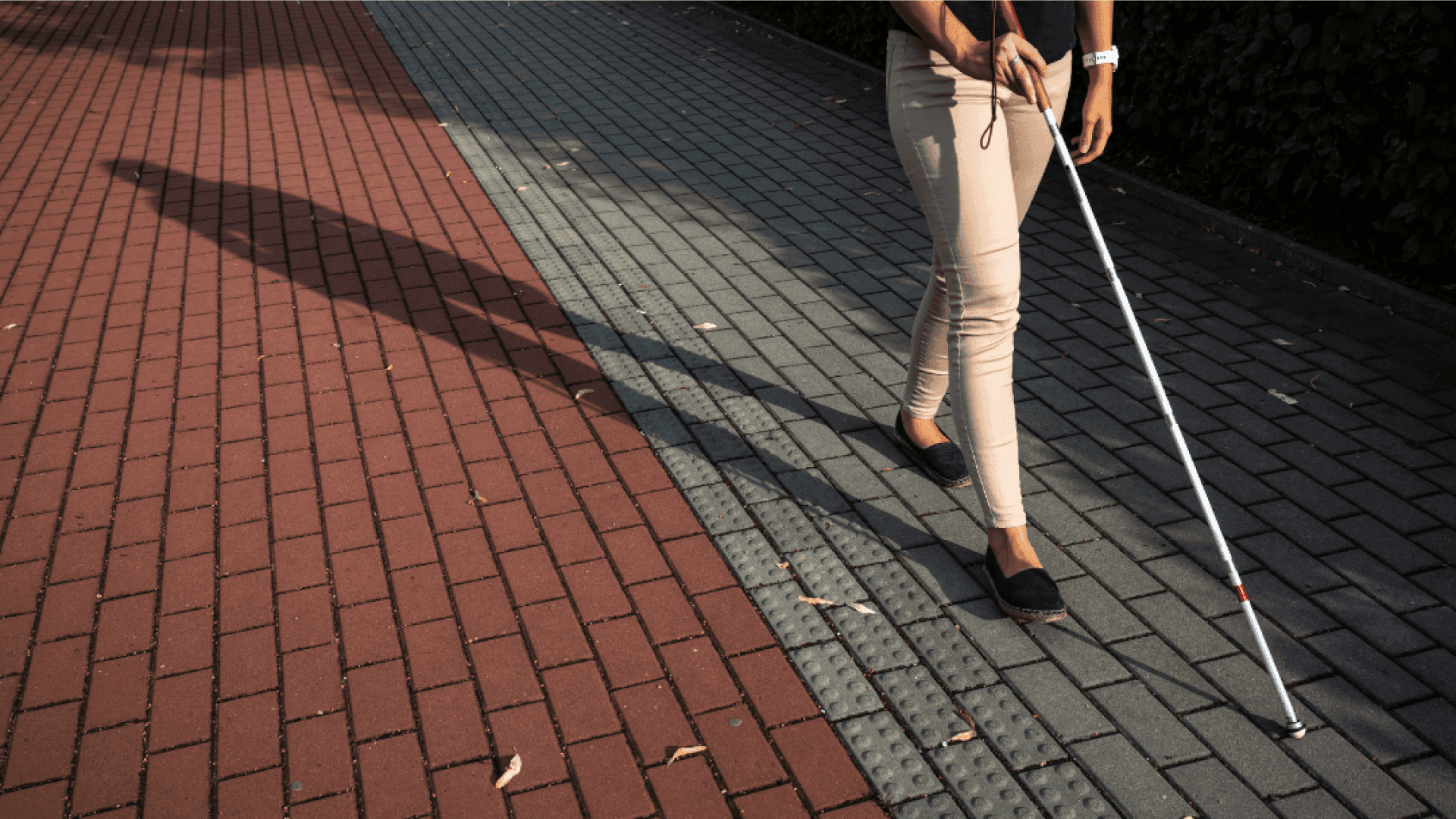 На фото зображено людину з порушенням зору, яка йде з палицею по дорозі На фото зображено людину з порушенням зору, яка йде з палицею по дорозі