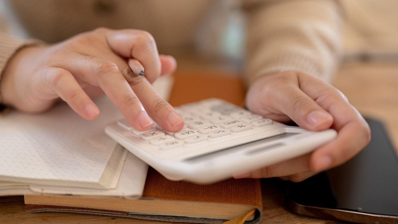 На фото руки людини рахують щось на калькуляторі На фото руки людини рахують щось на калькуляторі