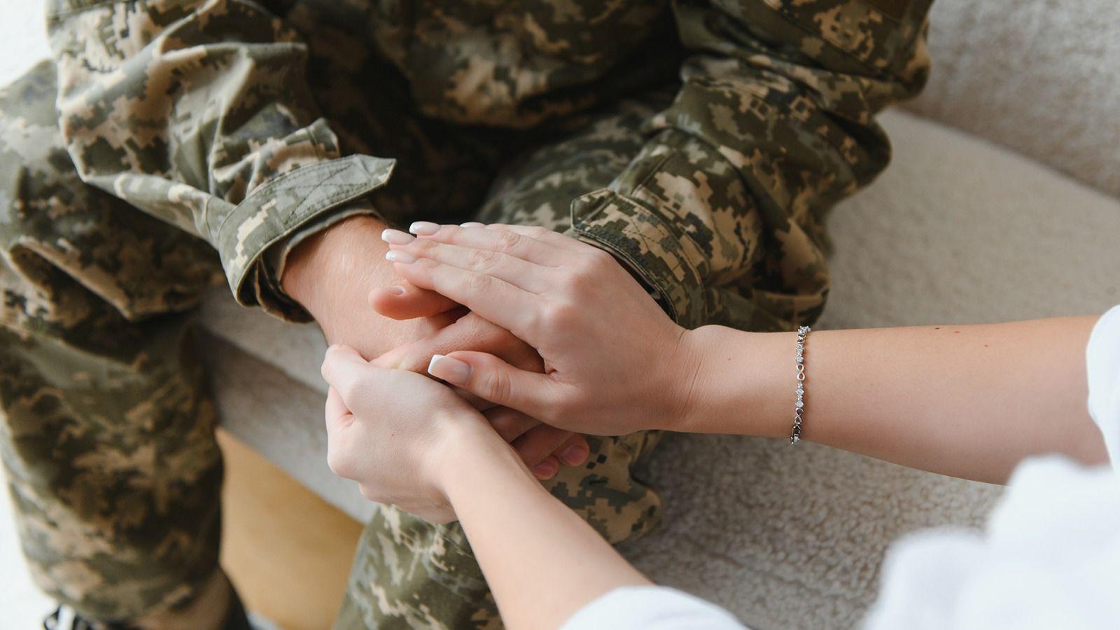 На фото людина тримає руки військовослужбовця На фото людина тримає руки військовослужбовця