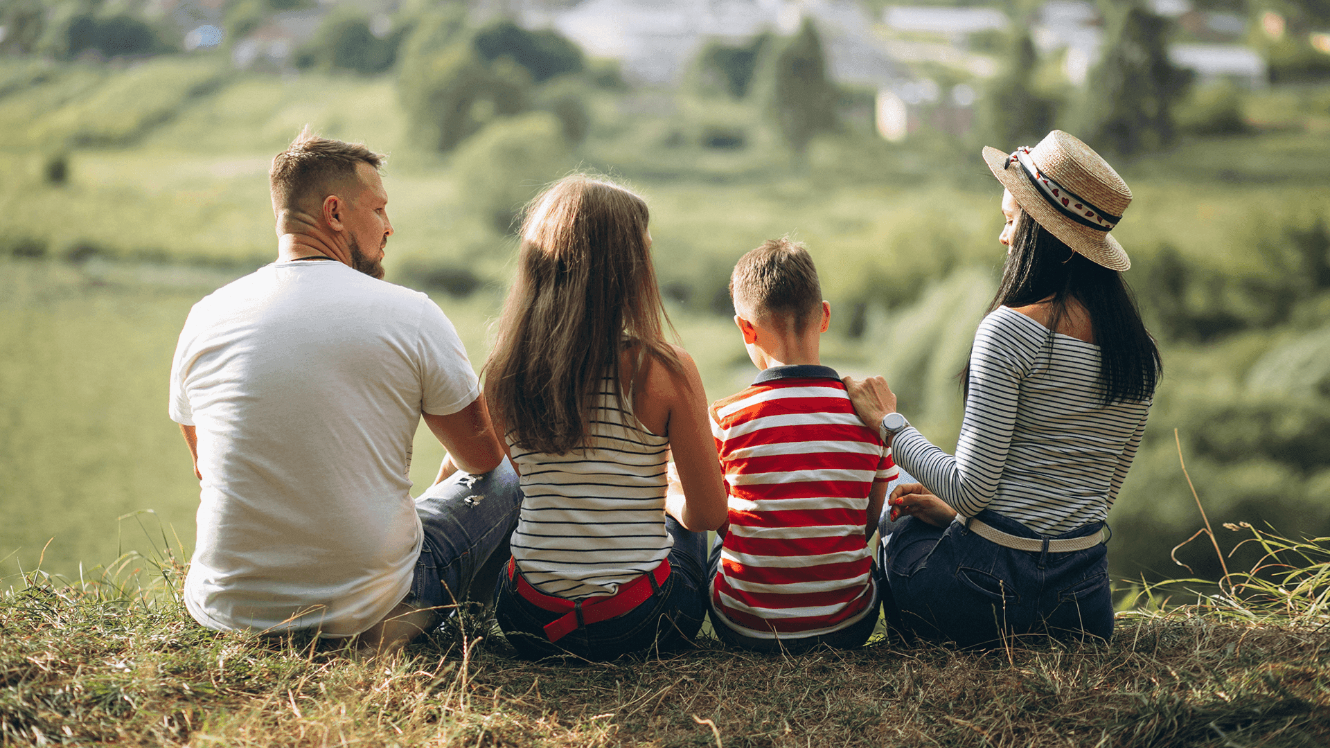 На зображенні чоловік, жінка і двоє дітей сидять на траві На зображенні чоловік, жінка і двоє дітей сидять на траві