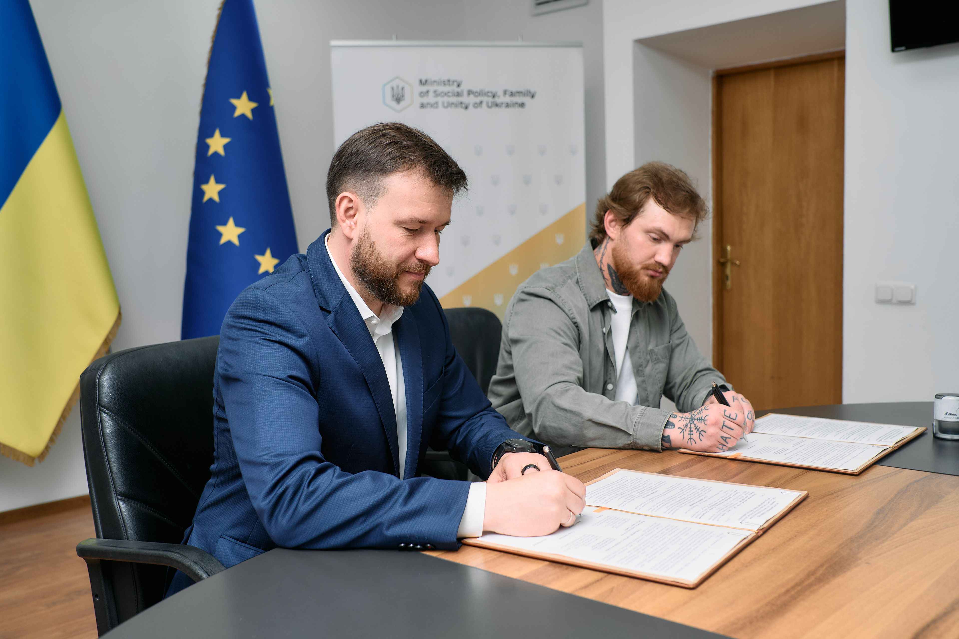 На фото чоловіки сидять за столом і підписують меморандум На фото чоловіки сидять за столом і підписують меморандум