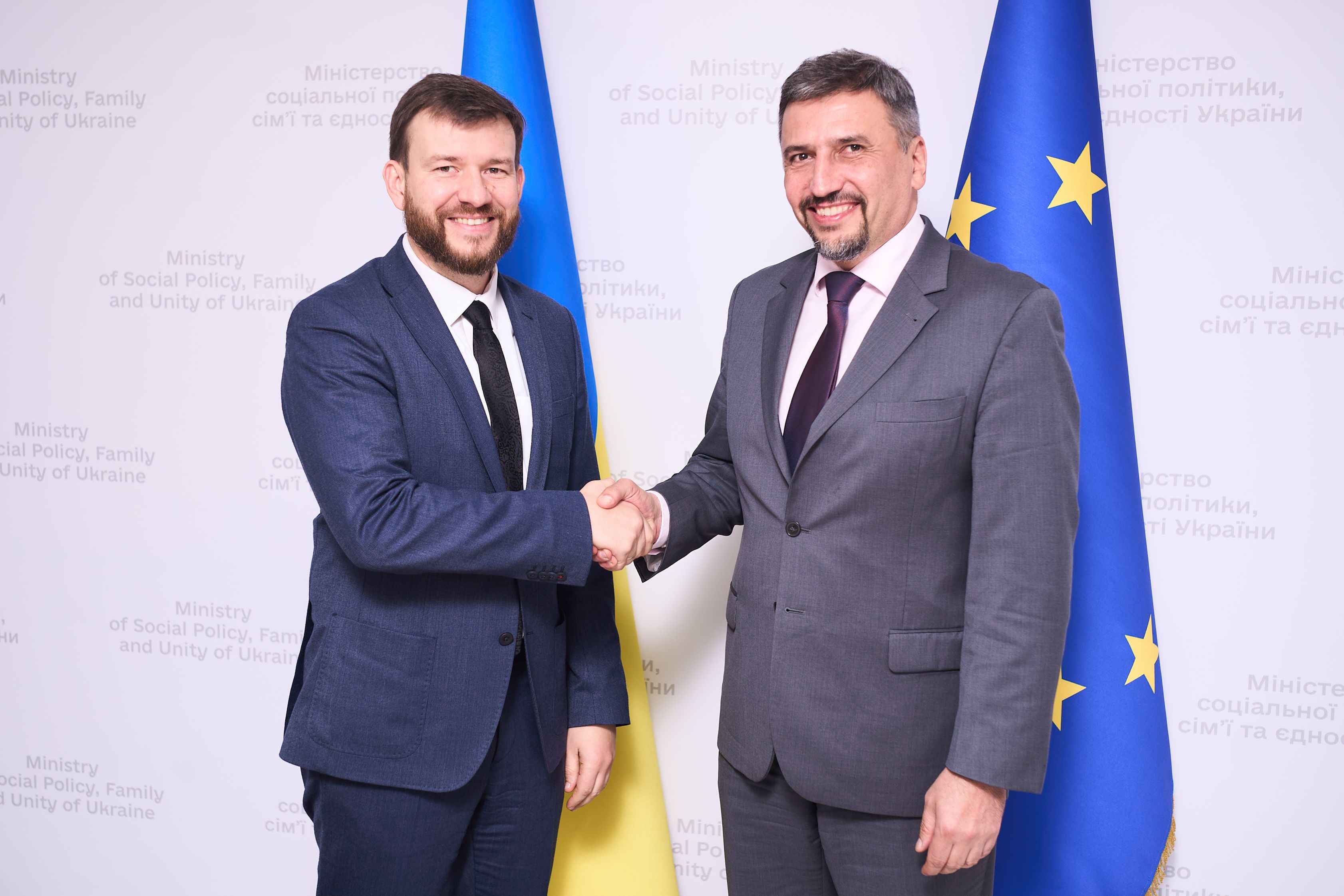 На фото чоловіки вітаються за руку і стоять на фоні прапорів України та ЄС На фото чоловіки вітаються за руку і стоять на фоні прапорів України та ЄС