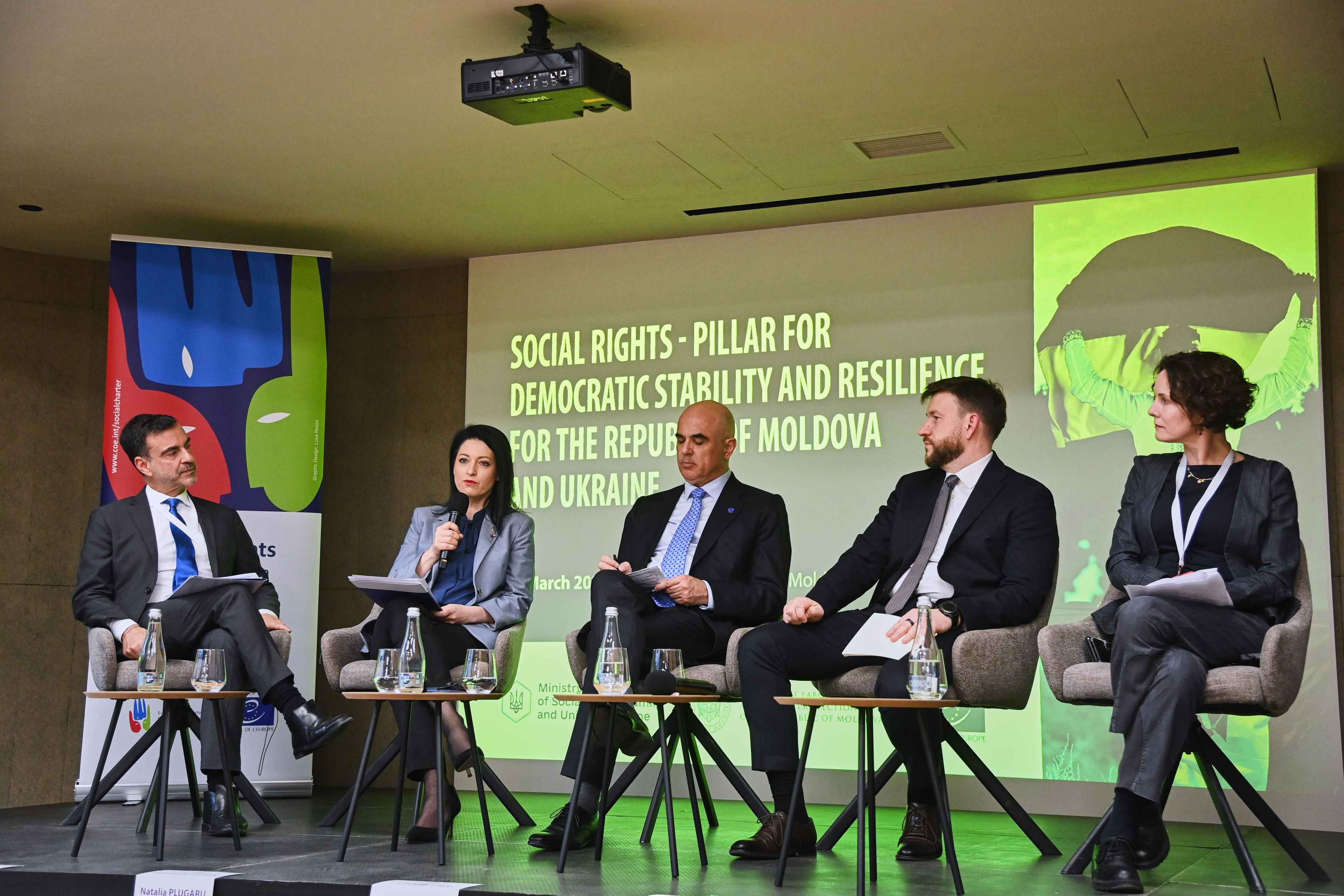 На фото жінки та чоловіки сидять у президії під час заходу На фото жінки та чоловіки сидять у президії під час заходу