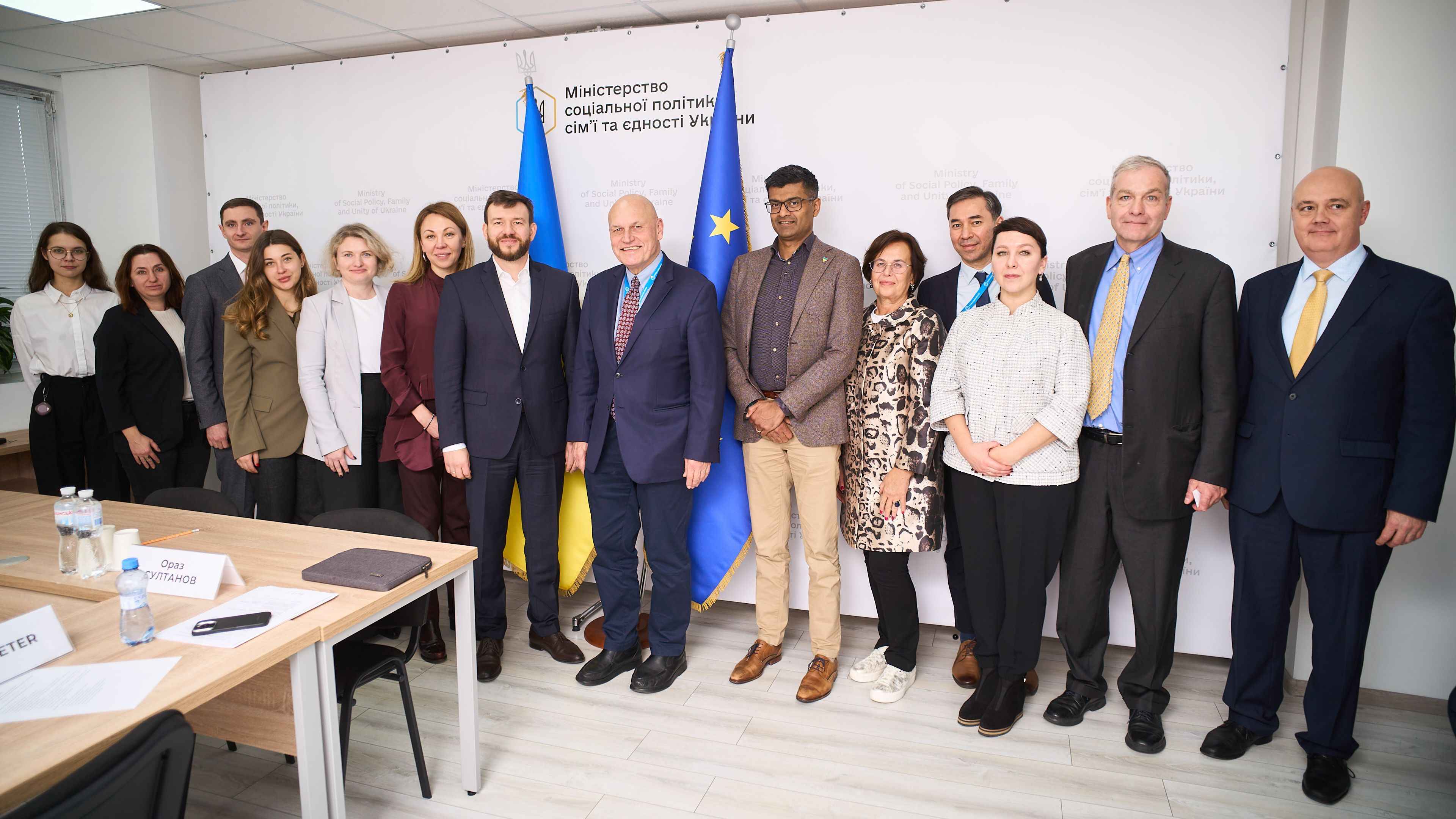 На фото чоловіки та жінки стоять після зустрічі на фоні прапорів України та ЄС На фото чоловіки та жінки стоять після зустрічі на фоні прапорів України та ЄС