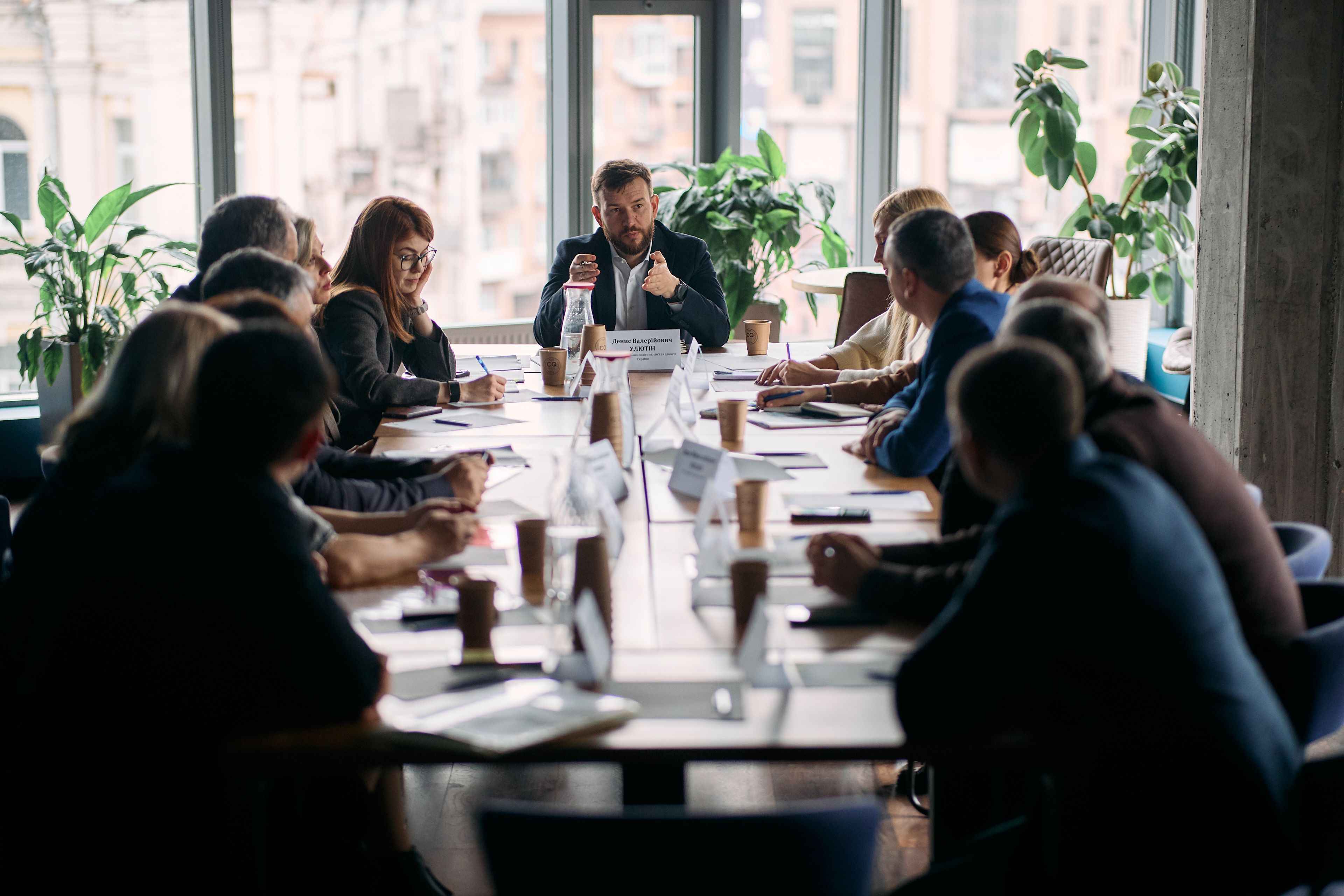 На фото чоловіки та жінки сидять за столом під час заходу На фото чоловіки та жінки сидять за столом під час заходу
