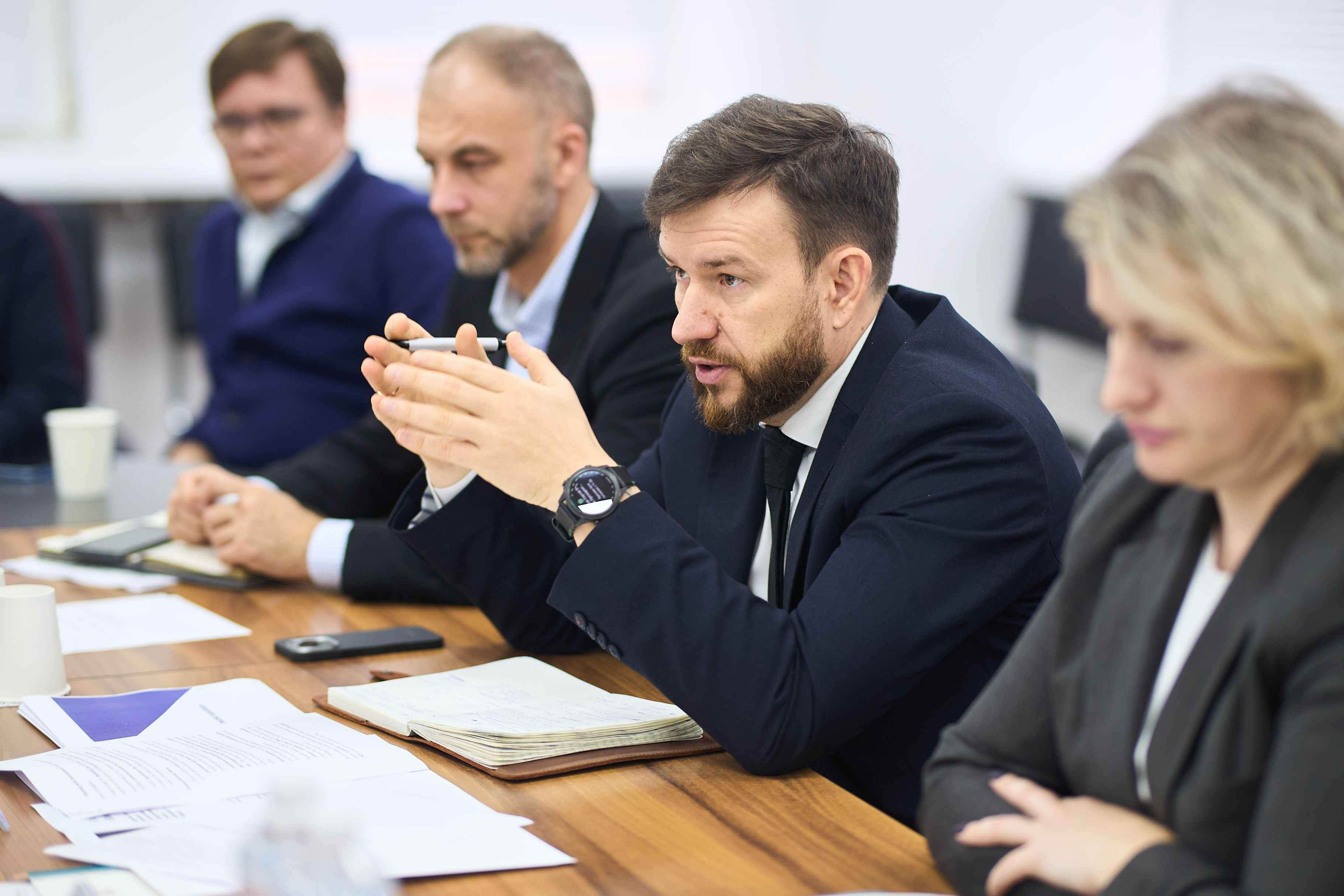 На фото чоловіки та жінка сидять за столом під час зустрічі На фото чоловіки та жінка сидять за столом під час зустрічі