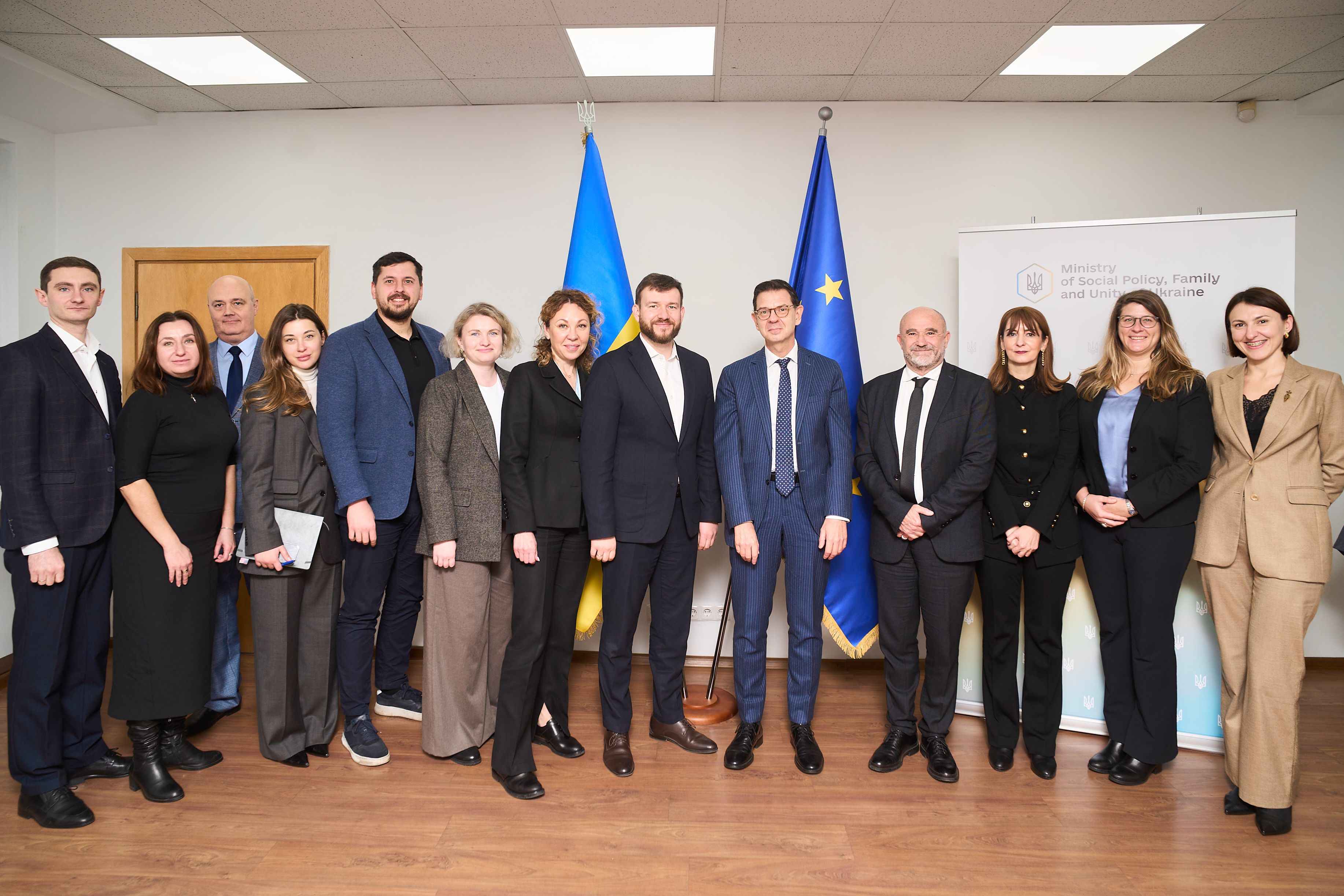 На фото жінки та чоловіки стоять на фоні прапорів України та ЄС На фото жінки та чоловіки стоять на фоні прапорів України та ЄС