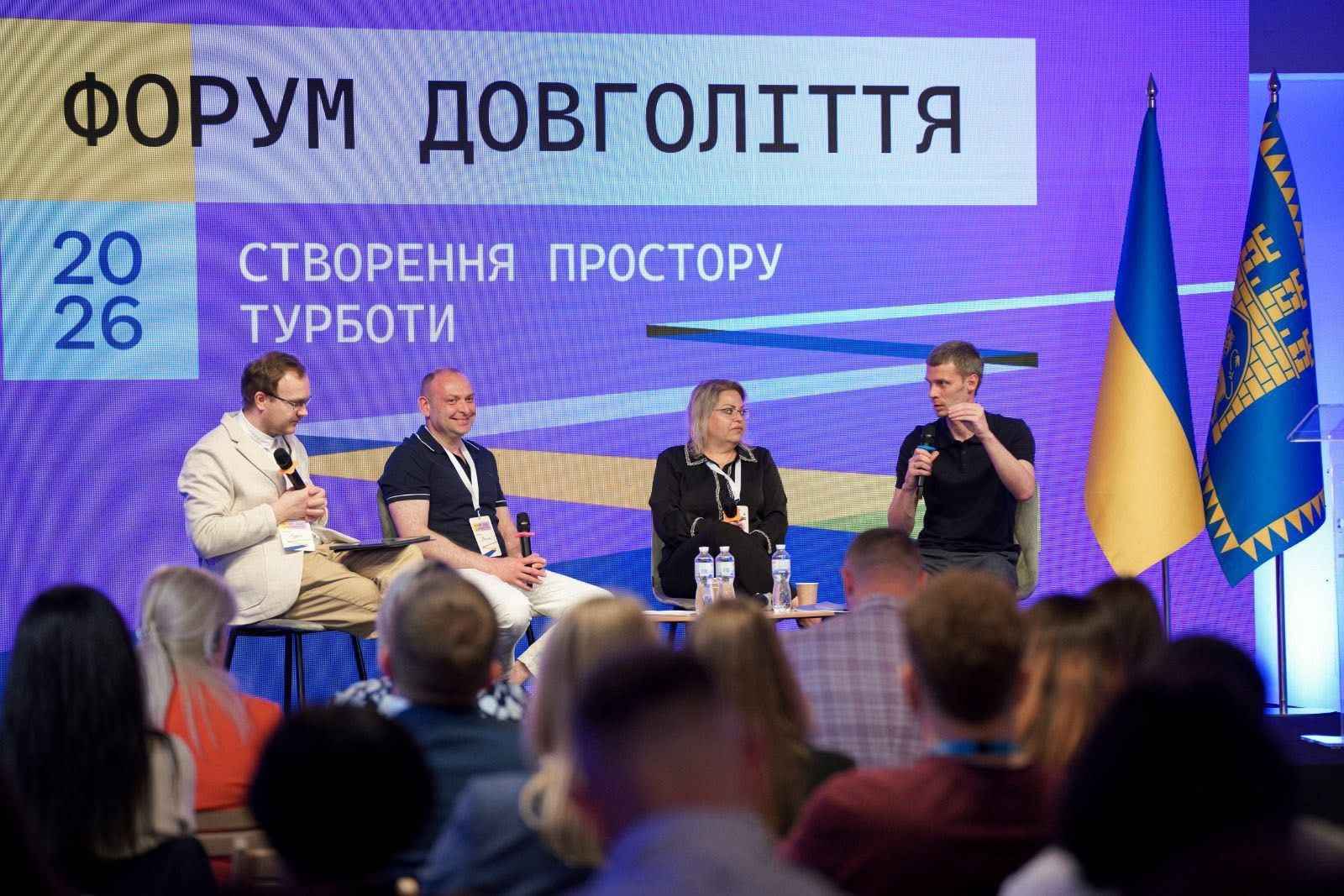 На фото жінки та чоловіки сидять на фоні банеру під час Форуму На фото жінки та чоловіки сидять на фоні банеру під час Форуму