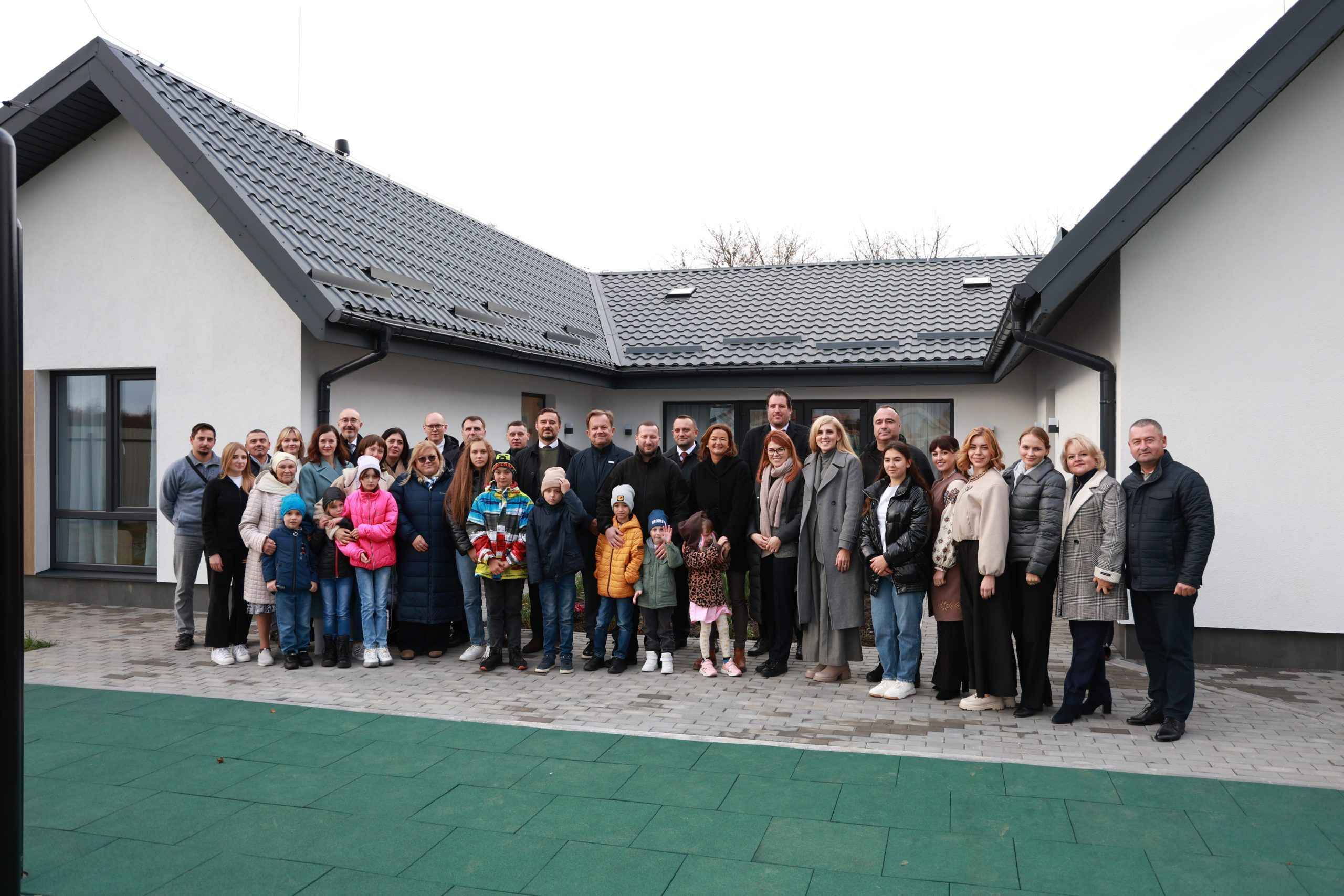 На фото жінки, чоловіки та діти стоять на фоні будинку На фото жінки, чоловіки та діти стоять на фоні будинку