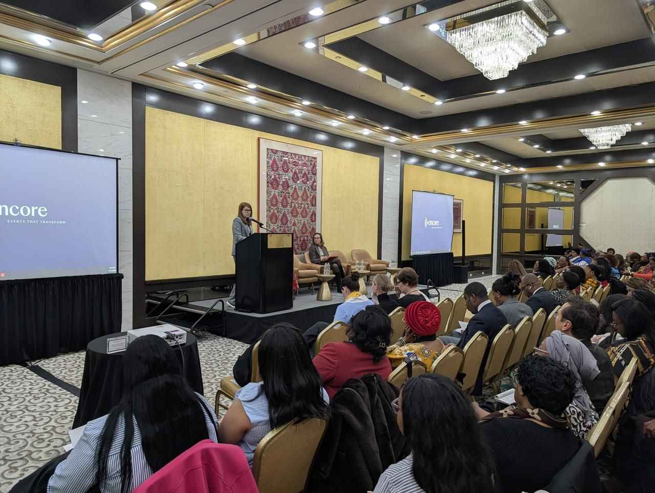 На фото жінки та чоловіки сидять в залі під час заходу На фото жінки та чоловіки сидять в залі під час заходу